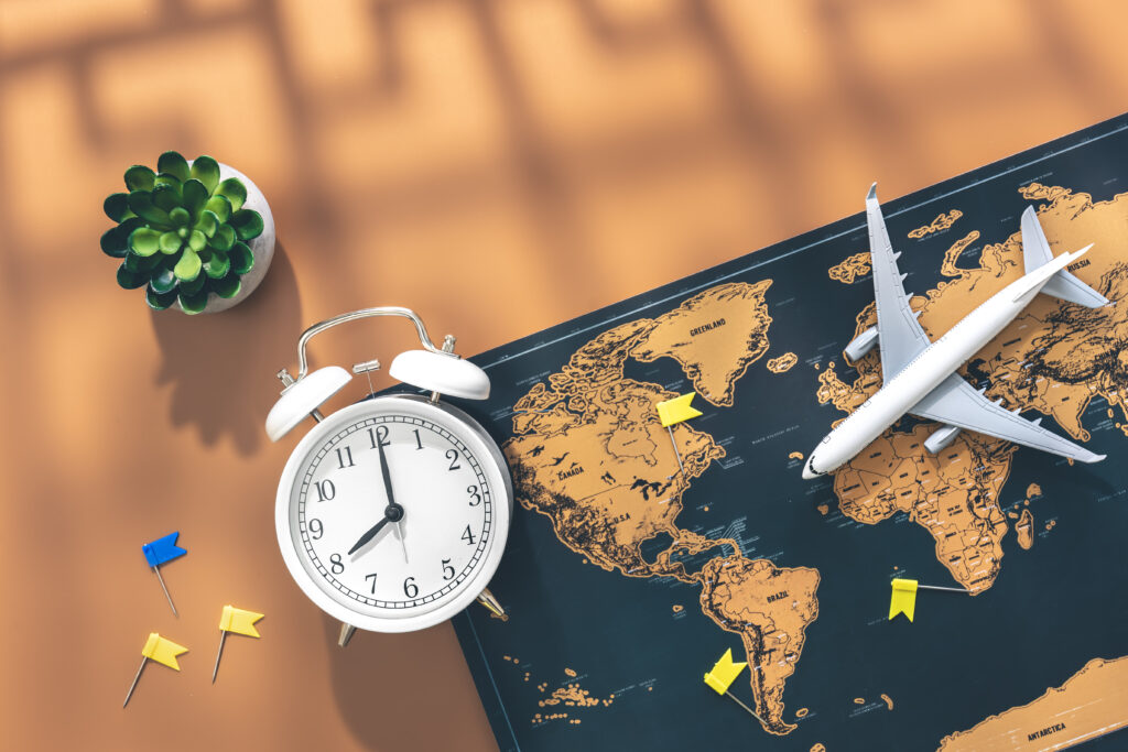 Alarm clock, airplane miniature and world map on brown background, flat lay.